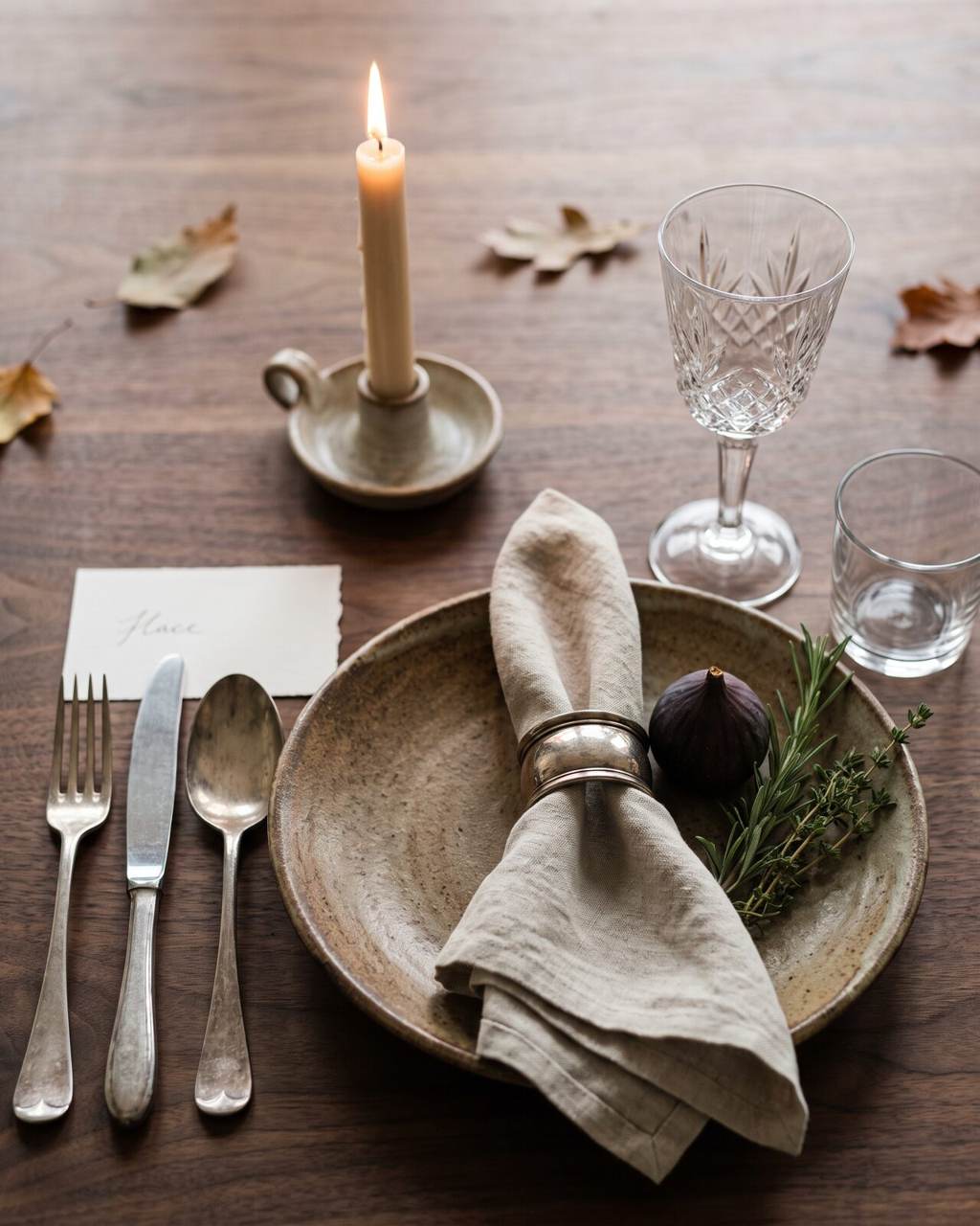 Close detail of one place setting: ceramic plate, linen napkin in an antique ring, patinated silver and crystal by candlelight