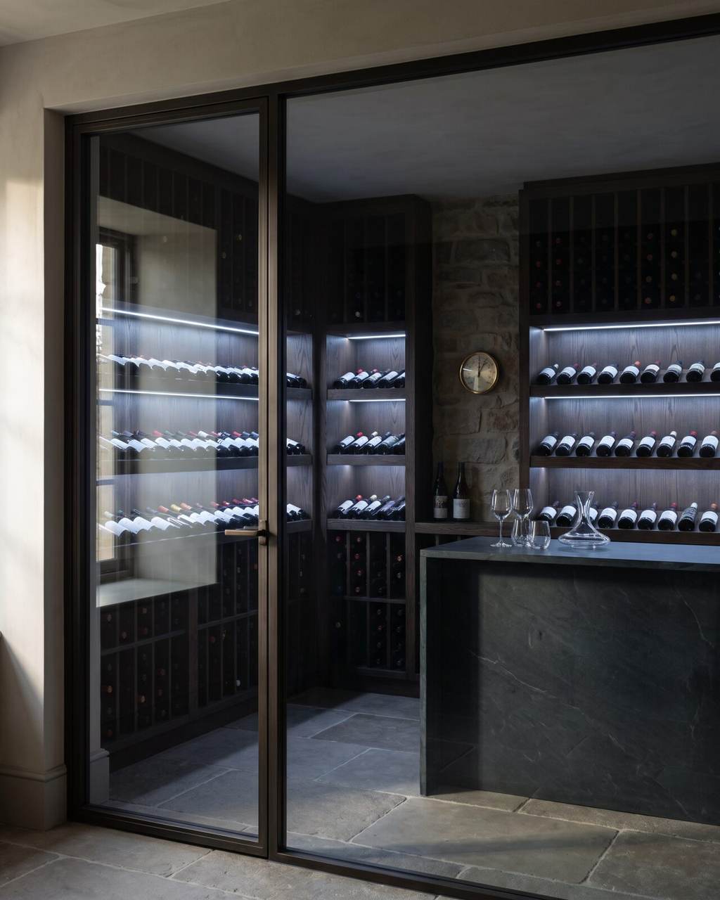 Conditioned wine room seen through glass, with dark oak racking, a stone tasting counter and a humidity gauge