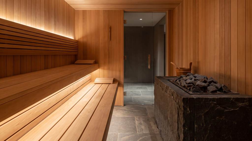 Interior of a residential heat room with wide clear-grade cedar benches, a basalt heater bed and concealed warm lighting under the upper bench