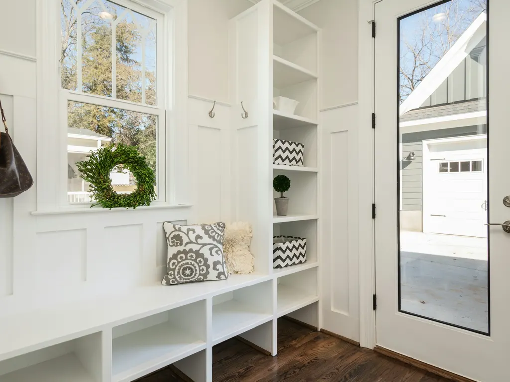 Bright white mudroom with a built-in bench, open cubbies, wall hooks and a glass door looking out to the garage